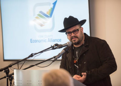 A man wearing glasses and a black hat is speaking into a microphone