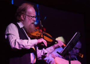 A bearded man with glasses is playing the violin at the 2018 YCEA dinner
