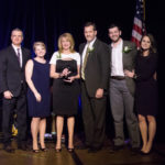 A group of three men in suits and three women in dresses are standing and holding an award during the 2018 YCEA dinner