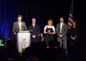 Three men and one woman stand beside a podium during the 2018 YCEA dinner