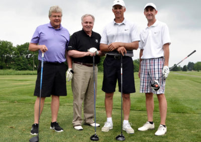 Four men wearing polo shirts are posing on a golf course