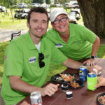 A man and women are both smiling and wearing green polo shirts at a golf course