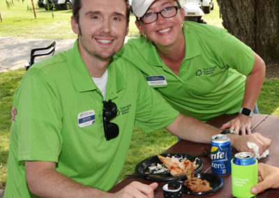 A man and women are both smiling and wearing green polo shirts at a golf course