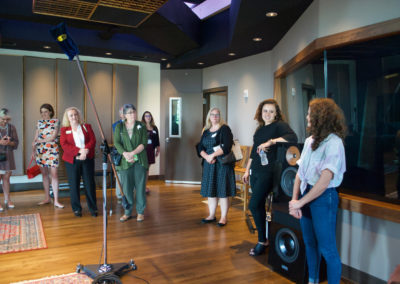 A group of six women are standing in a room with a wooden floor