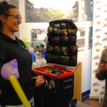 A woman wearing glasses and a black polo shirt is smiling in a store
