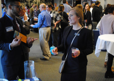 A woman in a black business suit is holding a cup of juice while speaking to a man in a black suit at a conference
