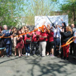 A large group of Casa members are celebrating and cutting an orange ribbon together in a parking lot