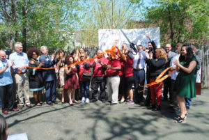 A large group of Casa members are celebrating and cutting an orange ribbon together in a parking lot