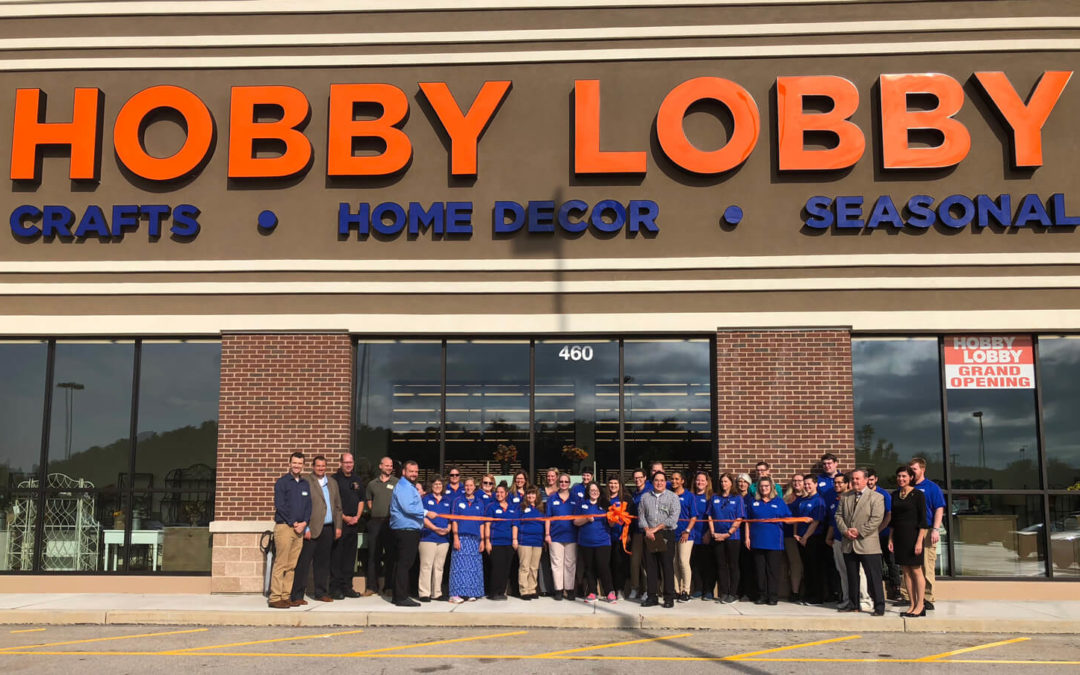 A group of Hobby Lobby workers are standing outside their store while holding a large orange ribbon