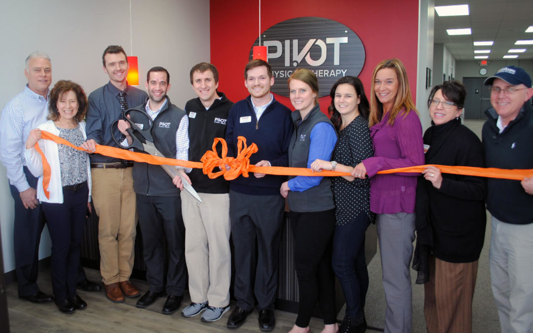 11 Pivot workers are standing and posing while holding a long orange ribbon
