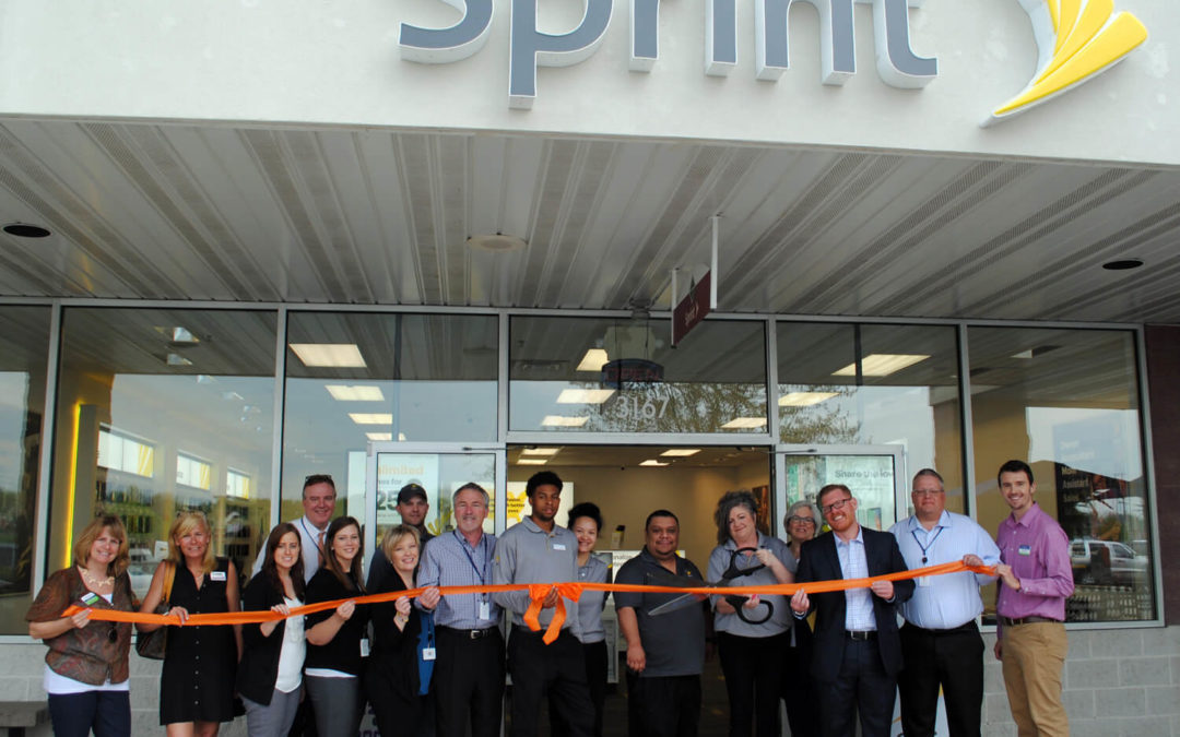 A group of Sprint workers are standing outside of their store while holding a long orange ribbon