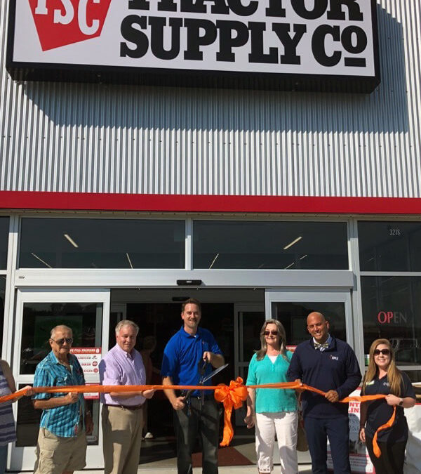 6 Tractor Supply workers are standing outside their store while holding a large orange ribbon